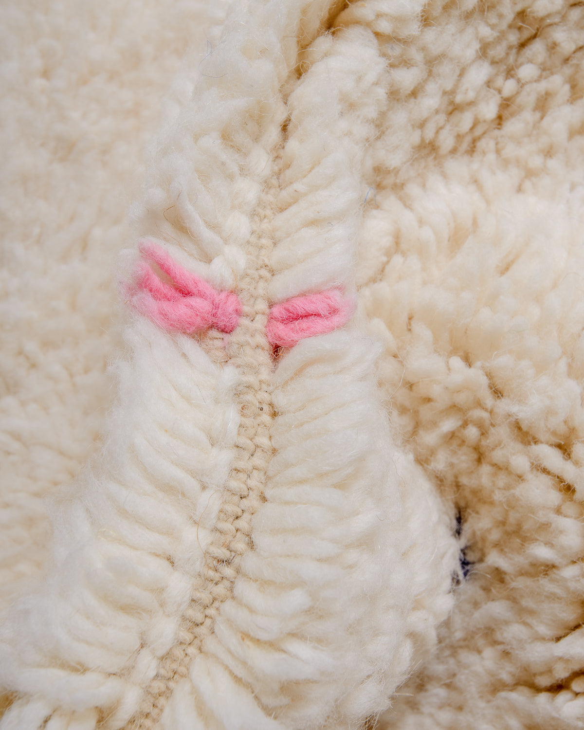 Close up of wool knots on rug in cream and pink.